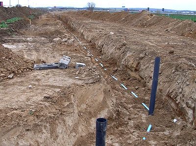 Rohrgraben in der Nähe des Gewerbegebietes Jacobsdorf Anhand der schwarzen Rohre kann der Vermesser sehen, wie tief die Leitung liegt. Sie werden später entfernt. Das blaue Warnband weist auf die Leitung hin.